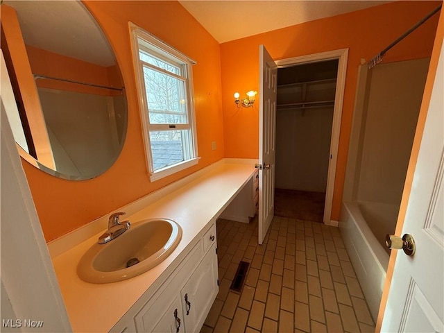 bathroom featuring brick floor, visible vents, bathing tub / shower combination, vanity, and a spacious closet