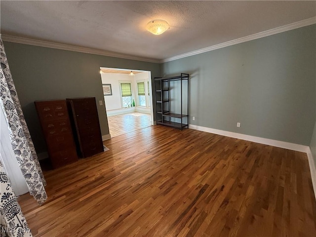 spare room featuring ornamental molding, a textured ceiling, baseboards, and wood finished floors