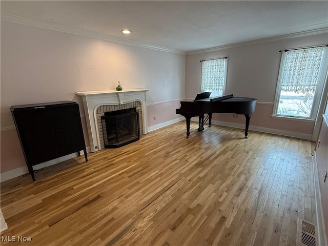 living area with light wood finished floors, visible vents, baseboards, ornamental molding, and a brick fireplace