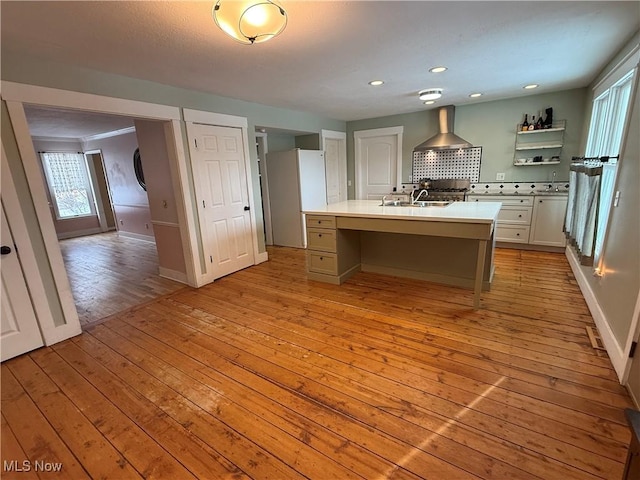 kitchen with a center island with sink, light wood finished floors, open shelves, light countertops, and a sink