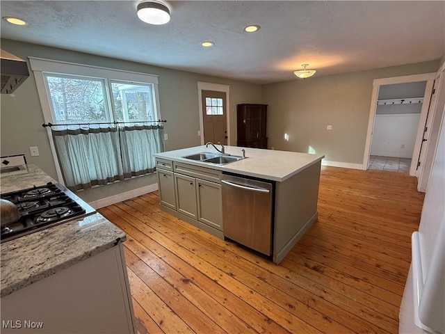 kitchen with light wood finished floors, a center island with sink, dishwasher, a sink, and black gas stovetop