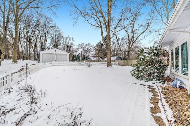 snowy yard featuring a detached garage, an outdoor structure, and fence