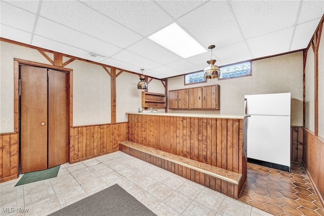 interior space with a wainscoted wall, a peninsula, light countertops, hanging light fixtures, and freestanding refrigerator