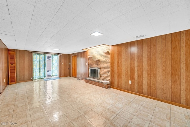 unfurnished living room with wooden walls, visible vents, baseboards, a brick fireplace, and light floors