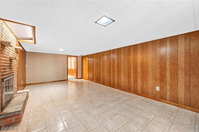 unfurnished living room with baseboards, a fireplace, wood walls, and light floors