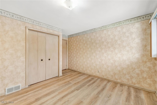 unfurnished bedroom featuring visible vents, baseboards, a closet, light wood-type flooring, and wallpapered walls