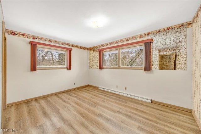 empty room featuring light wood-type flooring, baseboards, and a baseboard heating unit