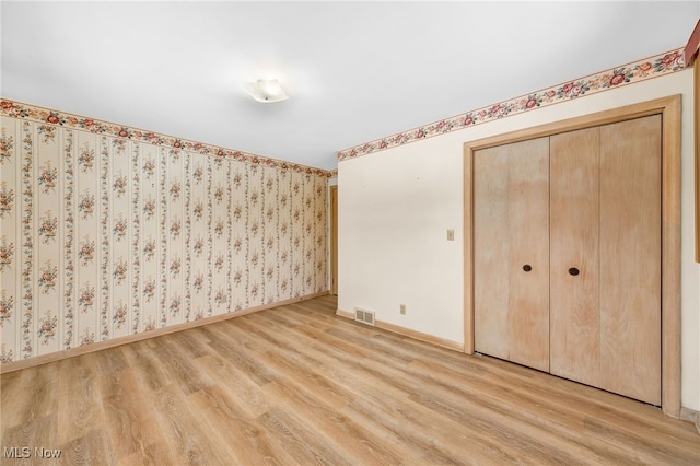 unfurnished bedroom featuring visible vents, light wood-style flooring, baseboards, and wallpapered walls