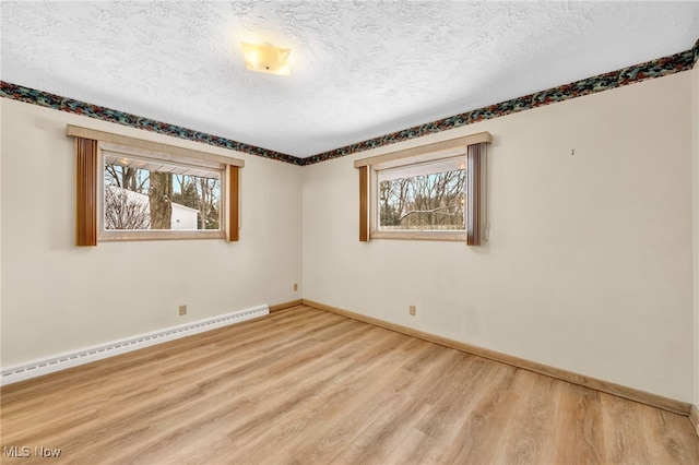 unfurnished room featuring light wood-style floors, a healthy amount of sunlight, a textured ceiling, and baseboard heating