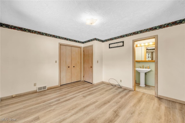 unfurnished bedroom with visible vents, light wood-style flooring, ensuite bathroom, a textured ceiling, and a sink