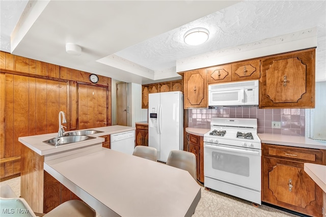 kitchen with brown cabinetry, white appliances, light countertops, and a sink