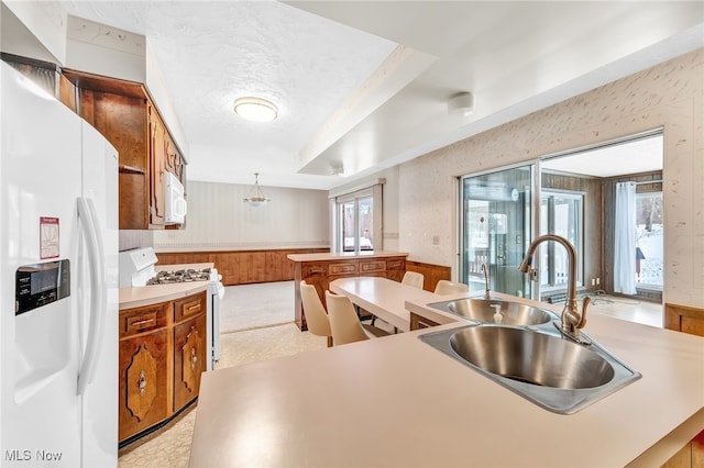 kitchen featuring light countertops, white appliances, a sink, and brown cabinets