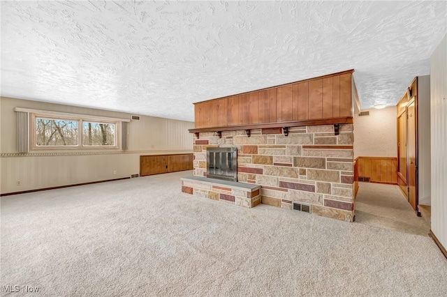 living room with visible vents, light carpet, wood walls, a stone fireplace, and a textured ceiling