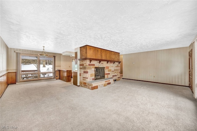 unfurnished living room featuring a textured ceiling, a stone fireplace, wood walls, and light colored carpet