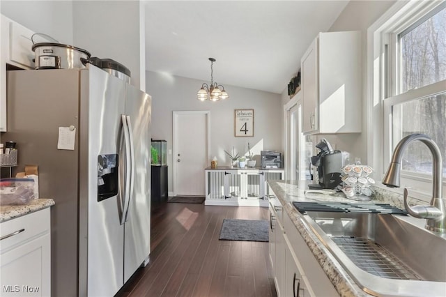 kitchen with lofted ceiling, hanging light fixtures, white cabinetry, stainless steel refrigerator with ice dispenser, and a sink