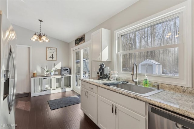 kitchen featuring white cabinets, lofted ceiling, decorative light fixtures, stainless steel appliances, and a sink