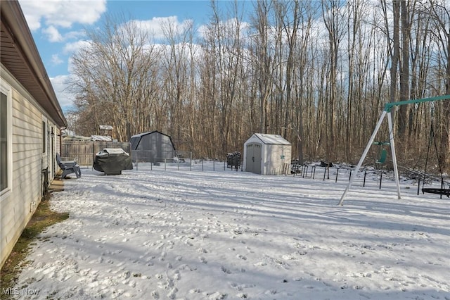 yard covered in snow featuring a storage shed, an outdoor structure, fence, and a playground