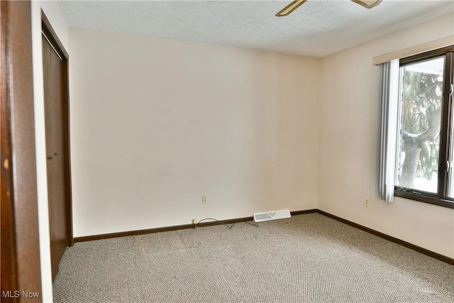 empty room with a textured ceiling, a ceiling fan, visible vents, baseboards, and carpet