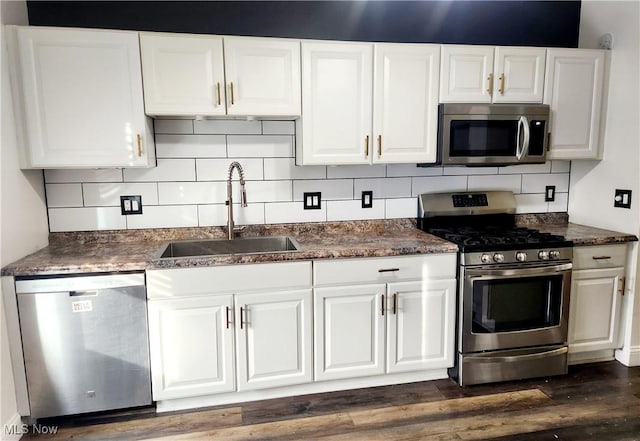 kitchen with dark countertops, white cabinetry, stainless steel appliances, and a sink