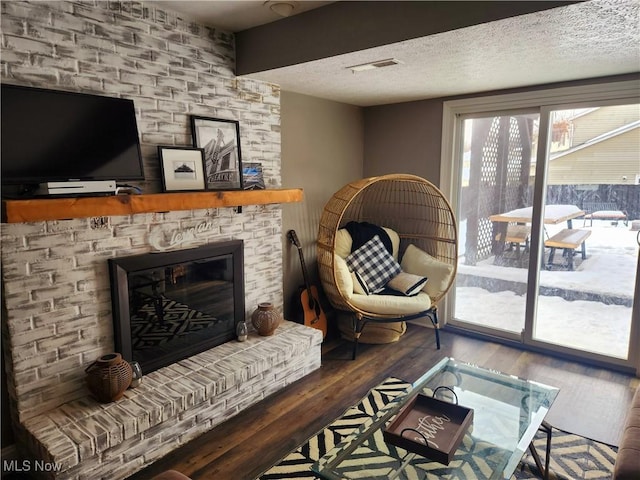 living area with a fireplace, visible vents, a textured ceiling, and wood finished floors