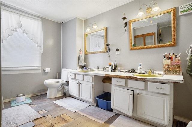 full bath with double vanity, a sink, toilet, and wood finished floors