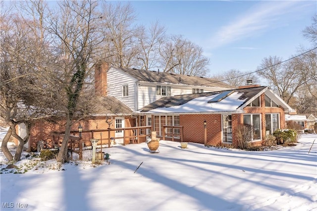 snow covered house with brick siding and a chimney