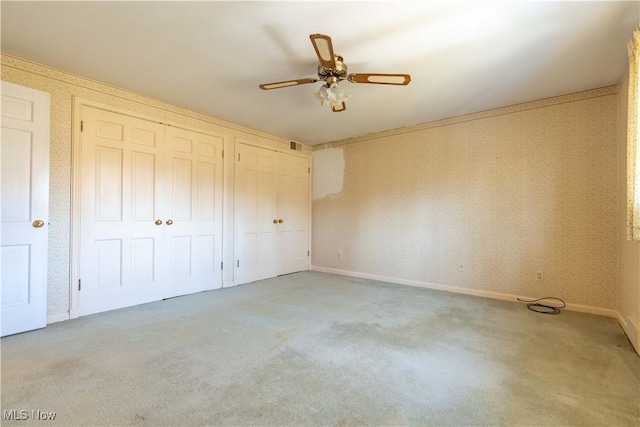 unfurnished bedroom featuring carpet, multiple closets, a ceiling fan, baseboards, and wallpapered walls