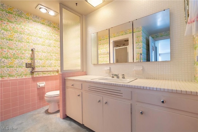 bathroom with toilet, a wainscoted wall, vanity, a shower stall, and tile walls