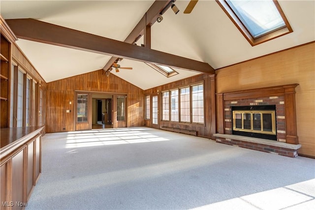 unfurnished living room featuring wood walls, carpet flooring, a ceiling fan, a brick fireplace, and lofted ceiling with skylight