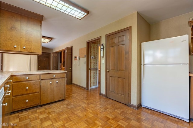 kitchen featuring light countertops, brown cabinetry, freestanding refrigerator, a peninsula, and baseboards