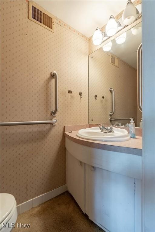 half bathroom with toilet, vanity, baseboards, visible vents, and wallpapered walls