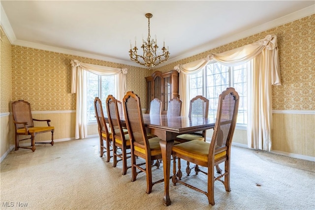 carpeted dining room with a wainscoted wall, ornamental molding, a chandelier, and wallpapered walls