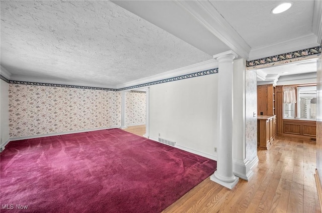 empty room with visible vents, crown molding, a textured ceiling, and ornate columns