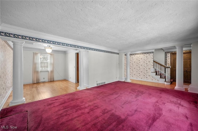 unfurnished living room featuring visible vents, crown molding, stairway, and ornate columns