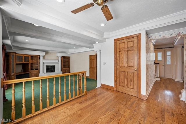 interior space with a fireplace with raised hearth, wood finished floors, baseboards, ornamental molding, and decorative columns