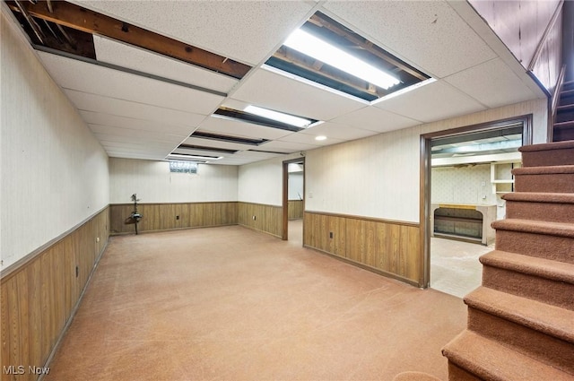 below grade area featuring a paneled ceiling, wainscoting, wood walls, and stairway