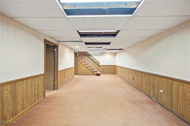 finished below grade area featuring a paneled ceiling, a wainscoted wall, wooden walls, and stairs