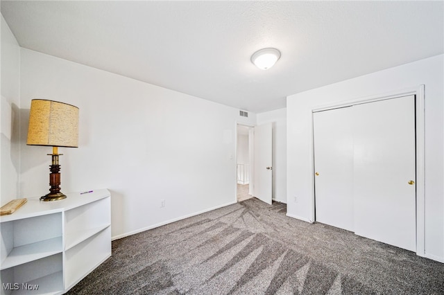 unfurnished bedroom featuring baseboards, visible vents, dark colored carpet, and a closet