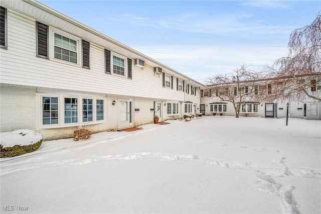 snow covered back of property featuring an AC wall unit and brick siding