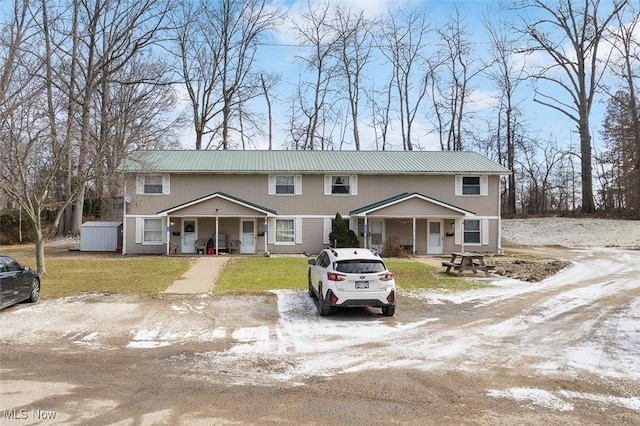 view of property with driveway, metal roof, a porch, and a front yard