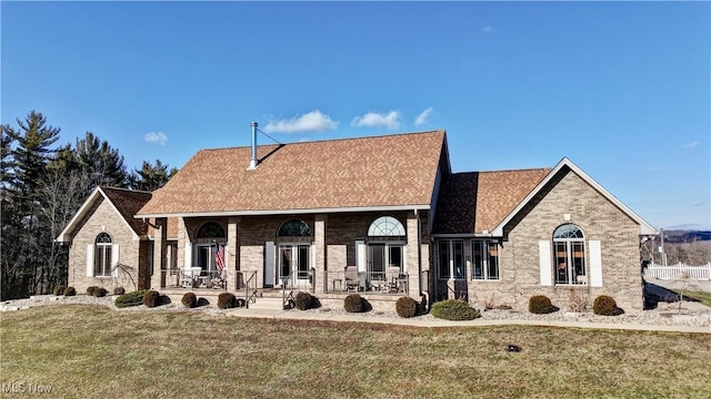 view of front of property with covered porch, brick siding, a front lawn, and roof with shingles