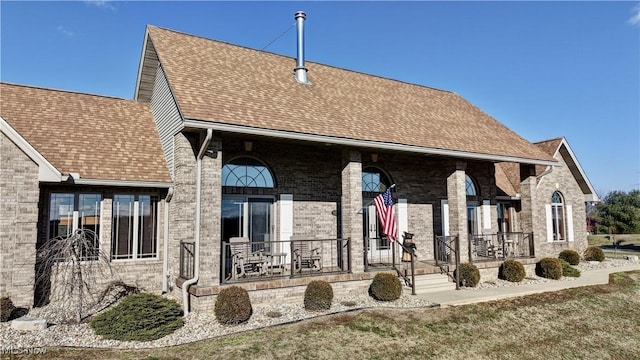 back of house with covered porch, a shingled roof, a lawn, and brick siding