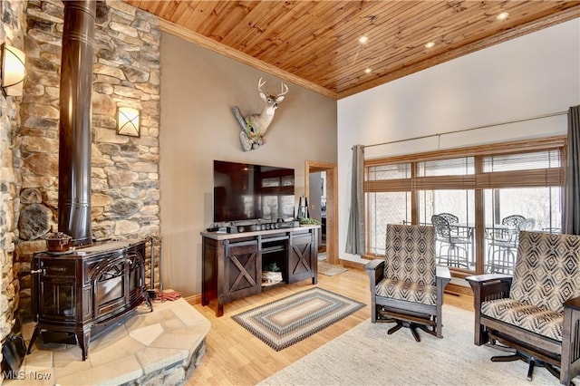 living area with wooden ceiling, ornamental molding, a wood stove, a high ceiling, and light wood-type flooring