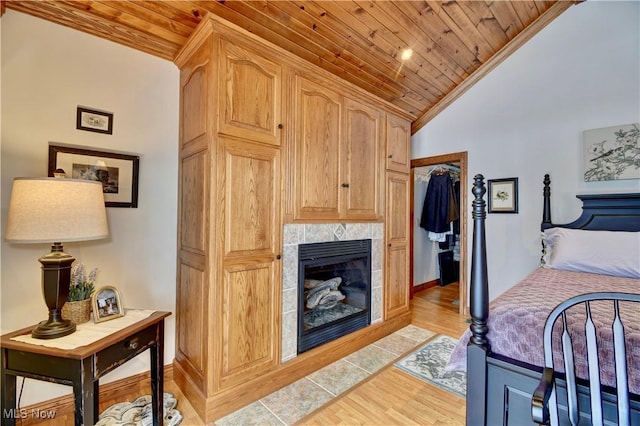 bedroom with lofted ceiling, a tile fireplace, wood ceiling, a spacious closet, and light wood finished floors