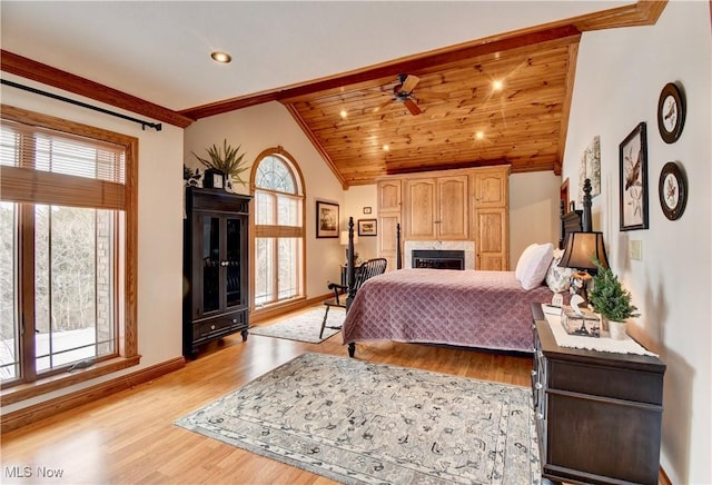 bedroom with lofted ceiling, a fireplace, baseboards, light wood-type flooring, and crown molding