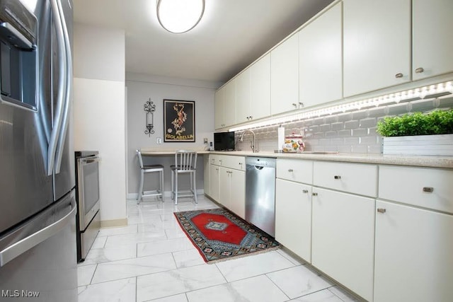 kitchen featuring marble finish floor, tasteful backsplash, light countertops, appliances with stainless steel finishes, and white cabinets