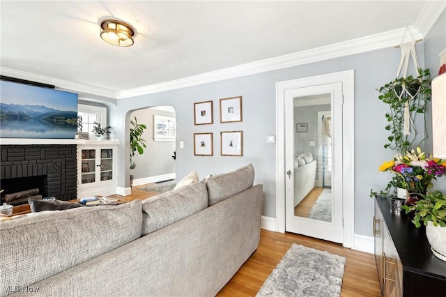 living room featuring arched walkways, a fireplace, baseboards, light wood finished floors, and crown molding