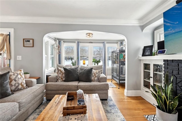 living room featuring arched walkways, a glass covered fireplace, crown molding, and wood finished floors