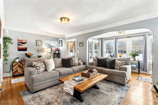 living area featuring arched walkways, baseboards, light wood-style flooring, and crown molding