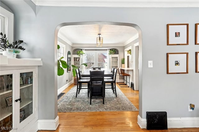 dining room featuring light wood-type flooring, arched walkways, ornamental molding, and baseboards